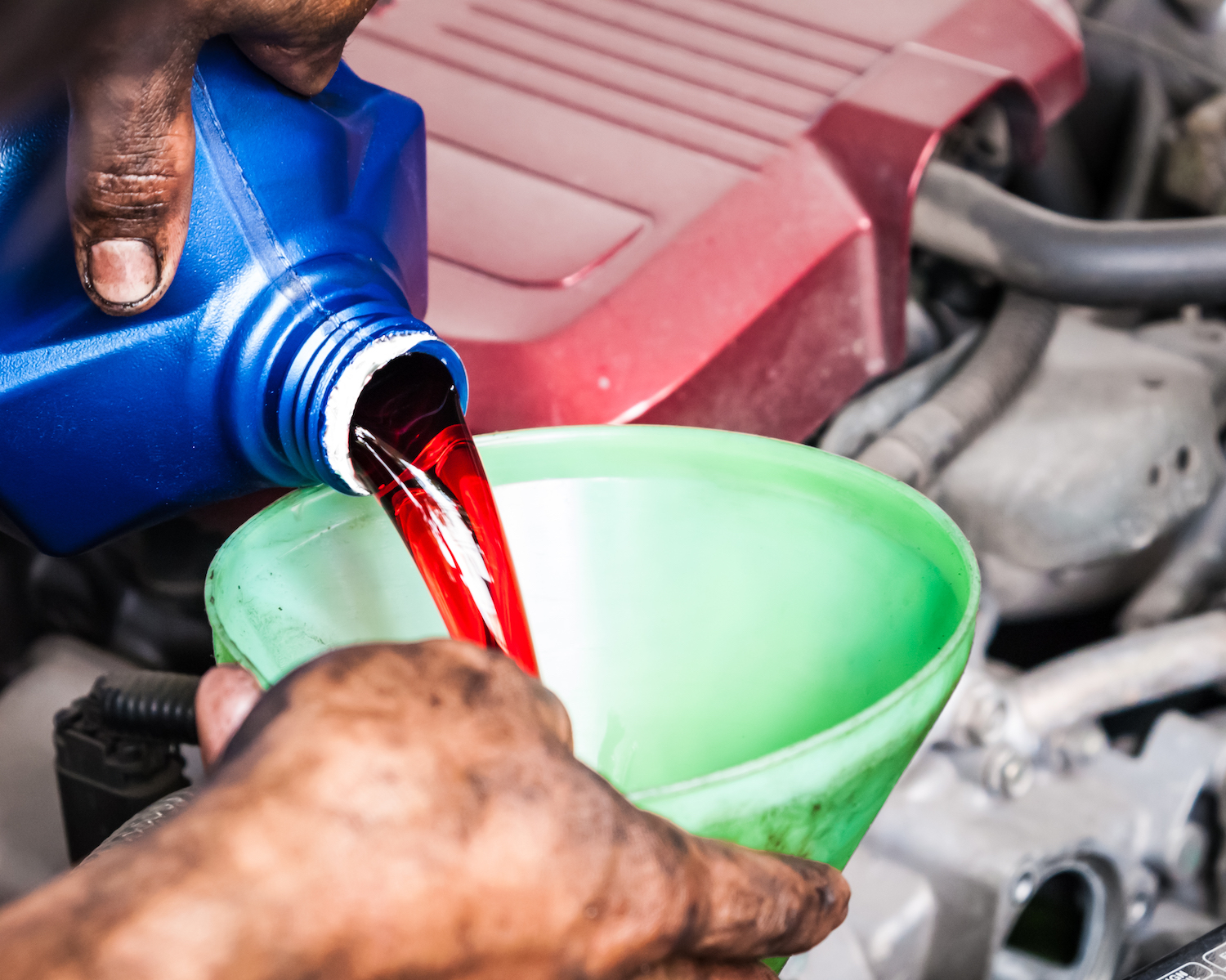 Man pouring transmission fluid through funnel into car